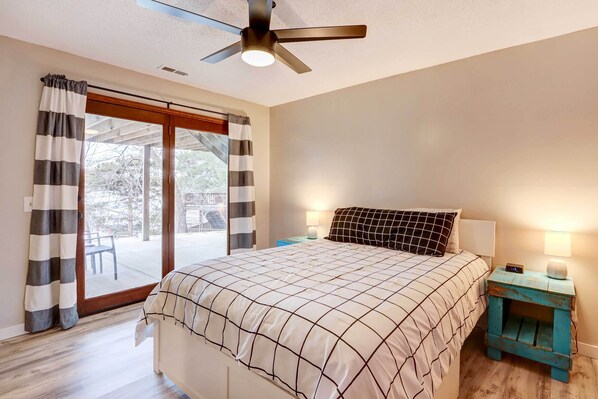 A bedroom with a bed, a ceiling fan, a nightstand with a lamp, and a view through a sliding glass door. - Dock, Deck & Views! Lakefront Retreat in Camdenton (Camdenton)