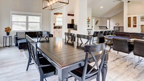 A spacious dining area with a long table and modern chairs, a kitchen in the background, and a ceiling fan. - Dock, Deck & Views! Lakefront Retreat in Camdenton (Camdenton)