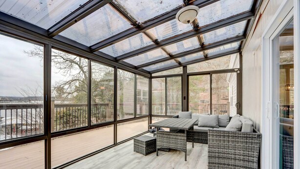 A sunroom with large glass windows, a wooden deck, and a seating area with a table and cushions. - Dock, Deck & Views! Lakefront Retreat in Camdenton (Camdenton)