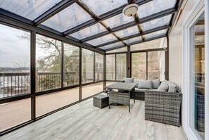 A sunroom with large glass windows, a wooden deck, and a seating area with a table and cushions. - Dock, Deck & Views! Lakefront Retreat in Camdenton (Camdenton)