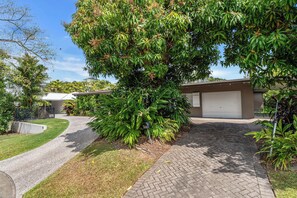A residential driveway leading to a house with a garage, surrounded by lush greenery and a well-maintained lawn.