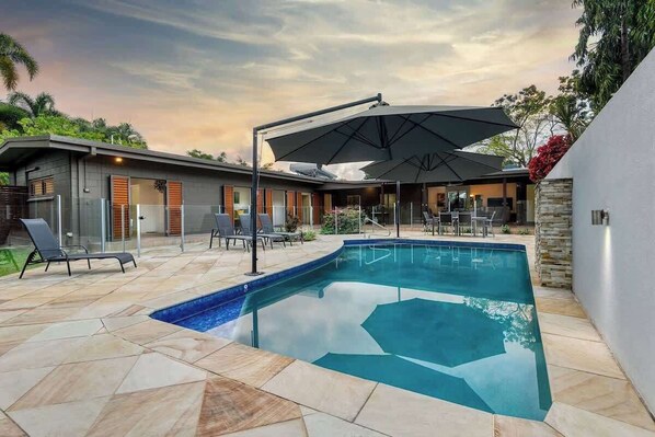 A modern outdoor pool area with a geometric tile design, lounge chairs, and umbrellas. - The Last Resort Bali House (Palm Cove)