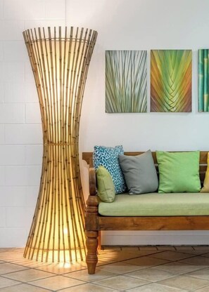 Una lampada da terra in bambù, un divano con cuscini e tre opere d'arte a parete.