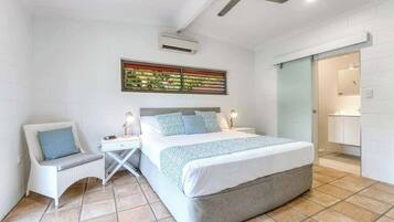 A bedroom with a bed, bedside tables, a chair, a ceiling fan, and a bathroom visible through an open door.