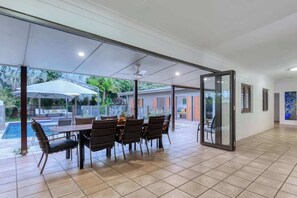 Un'ampia zona patio con tavolo e sedie, una porta vetrata che dà sull'esterno e vista su una piscina.
