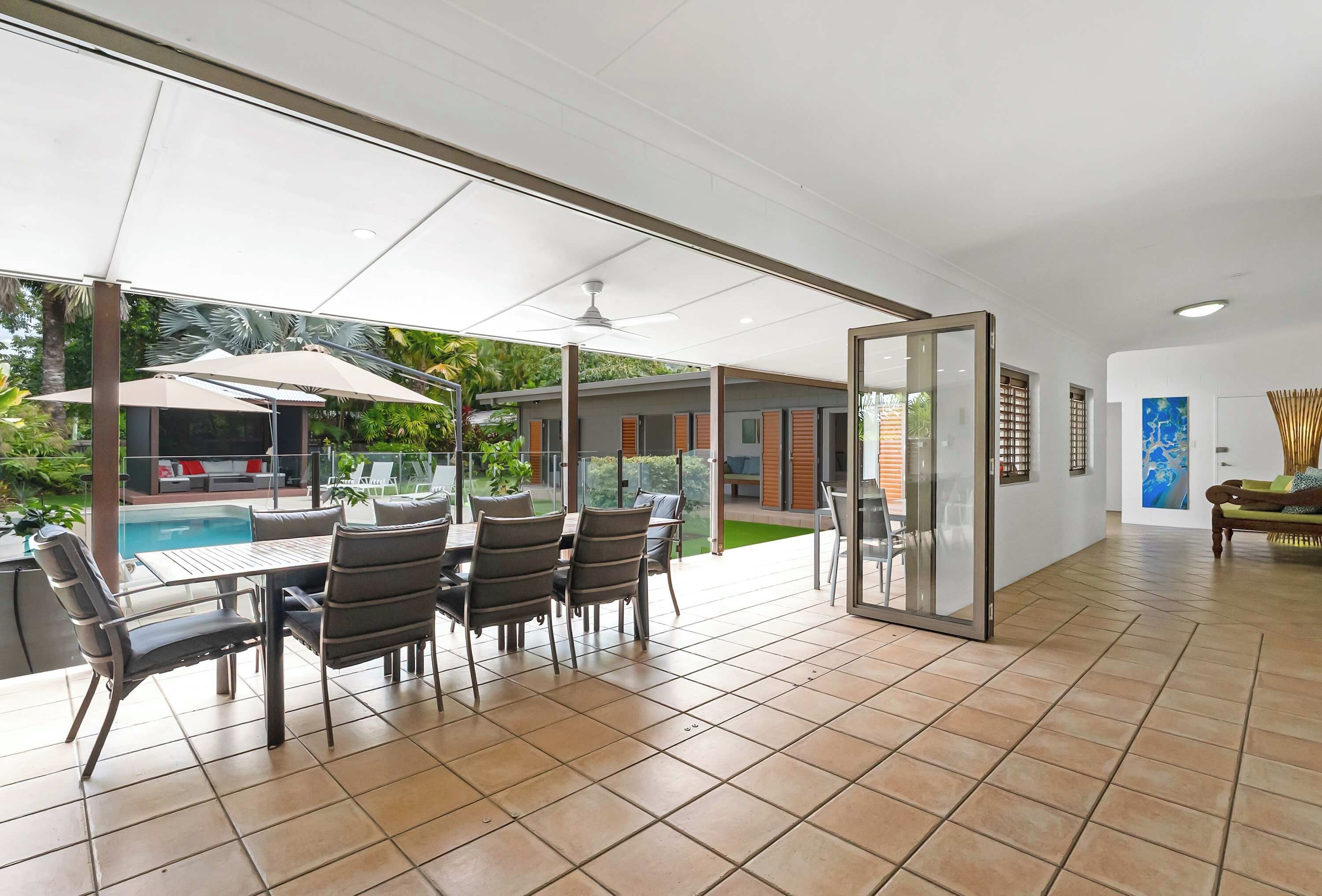 Un espace intérieur spacieux comprenant une table à manger et des chaises, un espace piscine visible à travers des portes vitrées et un ventilateur de plafond.