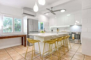 Una cucina moderna con isola centrale, sgabelli da bar, ventilatore a soffitto e un'ampia finestra con persiane.
