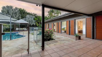 A modern outdoor patio with a swimming pool, glass doors, and a covered seating area.