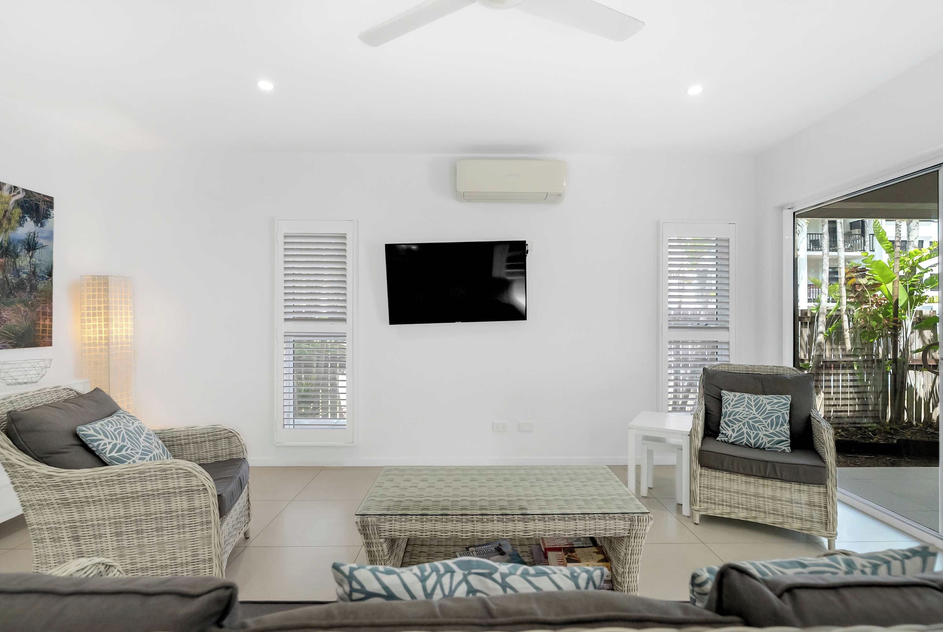 A living room with wicker furniture, a flat-screen TV, and a view through a glass door.