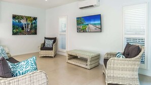 A room with wicker furniture, a ceiling fan, and two wall-mounted air conditioners.