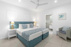 A modern bedroom with a bed, nightstands, a ceiling fan, and a bathroom visible through an open door. - The Last Resort - Villa 1 (Palm Cove)