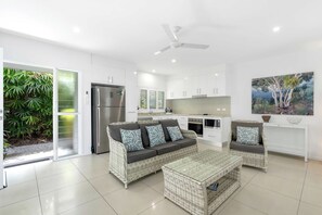 A modern kitchen with white cabinets, a stainless steel refrigerator, and a dining area with wicker furniture.
