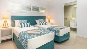 A hotel room with two beds, white nightstands, and a bathroom visible through an open door.
