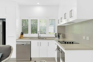 A modern kitchen with white cabinets, a dishwasher, a sink, and a stove.