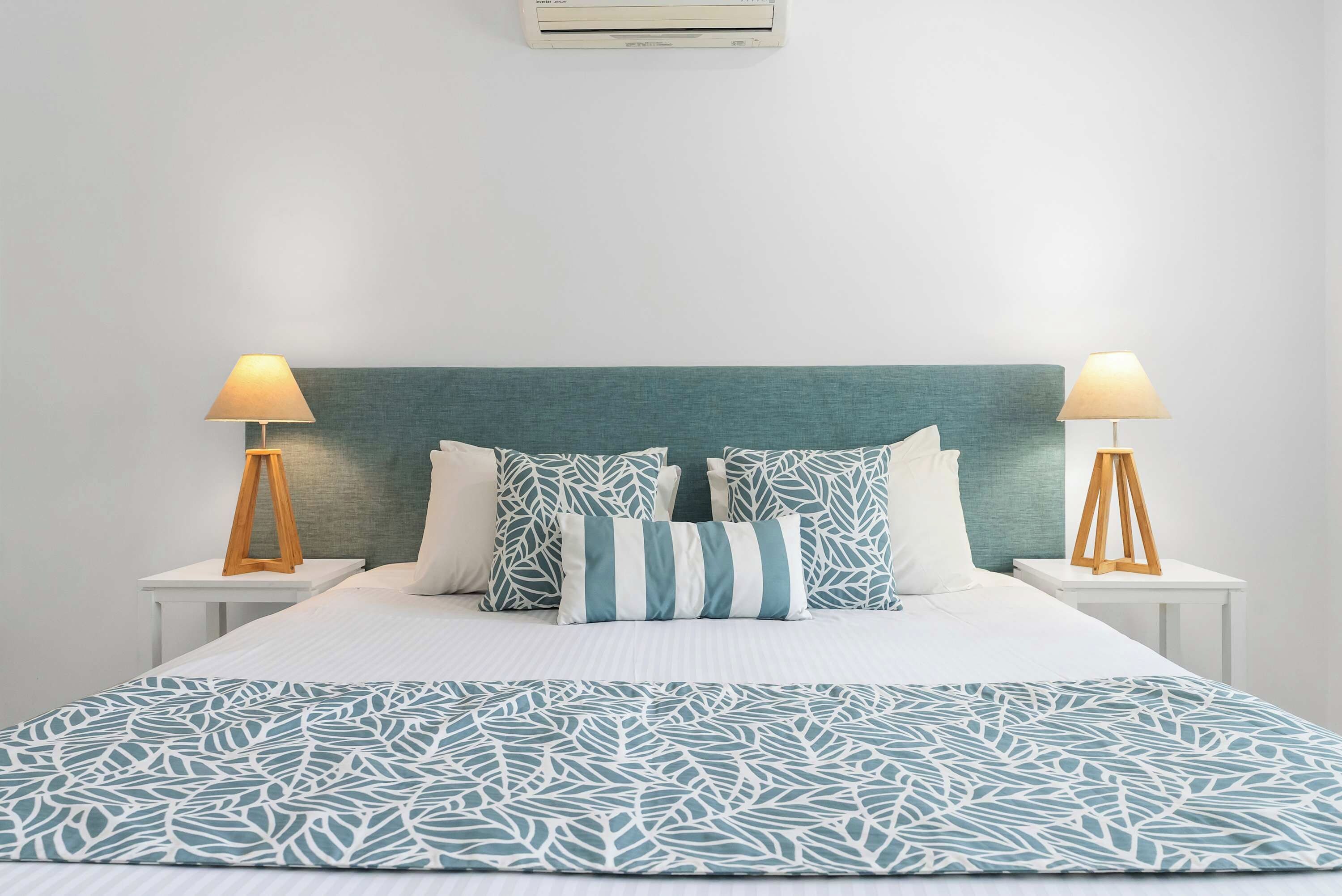 A bed with a teal headboard, white bedding, and patterned pillows. There are two bedside tables with lamps.