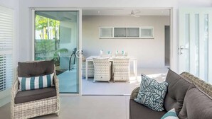 A modern living room with a sofa, a wicker chair, a dining table with chairs, and a sliding glass door leading to an outdoor area.