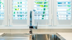 A kitchen with a stainless steel sink, a chrome faucet, and a window with blinds.