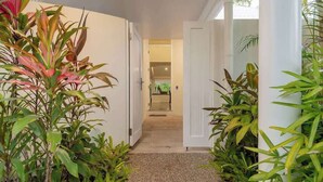 Un couloir avec des portes blanches, un sol carrelé et diverses plantes vertes.