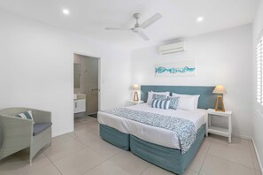 A bedroom with a bed, two bedside tables, a chair, a ceiling fan, and an air conditioning unit.