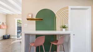 Zona de bar moderna amb dos tamborets rosos, un taulell blanc i una paret verda decorativa.