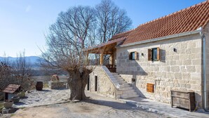A stone building with a red-tiled roof, a staircase leading to a porch, and a large tree in the foreground. - Nice home in Obrovac Sinjski with WiFi (Obrovac Sinjski)