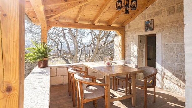 A wooden dining area with a table and chairs, a potted plant, and a stone wall. - Nice home in Obrovac Sinjski with WiFi (Obrovac Sinjski)