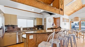 A modern kitchen with a central island, bar stools, and a dining area with natural light.