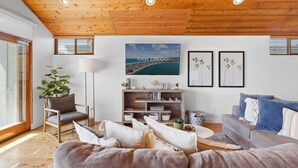 A living room with a wooden ceiling, a sofa, a coffee table, a bookshelf, and a large window.
