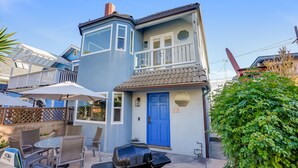 Una casa de dos pisos con una puerta azul, un balcón y un patio con mobiliario exterior.