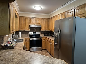 A kitchen with wooden cabinets, a stainless steel refrigerator, a microwave, a stove, and a sink.