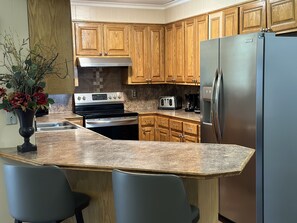 A kitchen with wooden cabinets, a stainless steel refrigerator, a stove, and a toaster. - Spacious home/outdoor area minutes from Amazon Center, LSU, SU, downtown & mall (Baton Rouge)