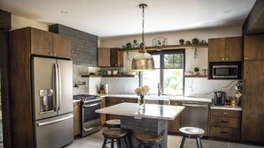 Une cuisine moderne dotée d’un îlot central, de tabourets de bar, d’appareils électroménagers en acier inoxydable et de meubles de rangement en bois.