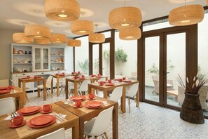 A dining area with wooden tables and chairs, wicker pendant lights, and a view of the outdoors through large windows. - Hotel Boutique Lambassade Bellavista (Santiago)