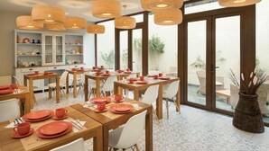 A dining area with wooden tables and chairs, wicker pendant lights, and a view of the outdoors through large windows.