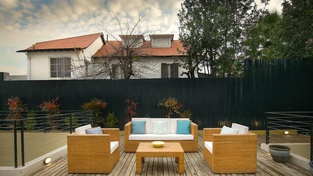 An outdoor patio with wicker furniture, a wooden table, and a view of a house in the background.