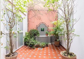Un patio con suelo de baldosas, plantas en macetas y una pared de cerámica con un diseño geométrico.