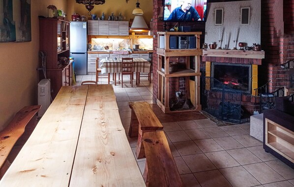 A rustic kitchen with a long wooden table, a brick fireplace, and a television mounted on the wall. - Nice home in Raków with sauna (Raków)
