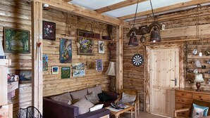 A rustic wooden room with a sofa, a wooden cabinet, and various wall decorations including framed pictures and a dartboard. - Nice home in Raków with sauna (Raków)