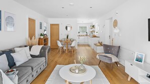 A modern living room with a grey sofa, a dining table, and a kitchen in the background. - Plover 1, The Cove - On site pool - Wi-Fi (Brixham)