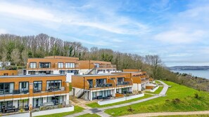 A modern residential building with multiple floors, large windows, and a view of a lake. - Plover 1, The Cove - On site pool - Wi-Fi (Brixham)