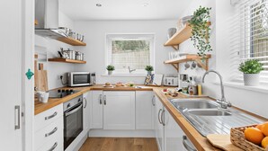 A compact kitchen with white cabinets, a wooden countertop, a built-in oven, a microwave, a sink, and various kitchen utensils and appliances. - Plover 1, The Cove - On site pool - Wi-Fi (Brixham)