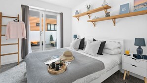 A modern bedroom with a bed, bedside tables, a wardrobe, and a view of the outside. - Plover 1, The Cove - On site pool - Wi-Fi (Brixham)