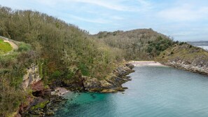 A coastal landscape with a rocky shoreline, a clear blue sea, and a forested hill. - Plover 1, The Cove - On site pool - Wi-Fi (Brixham)