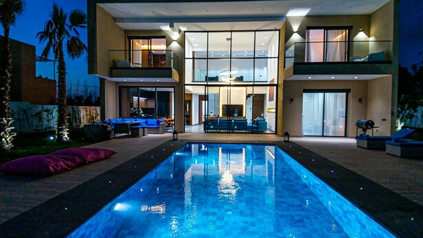 Een modern huis met twee verdiepingen, een zwembad, buitenzitplaatsen en een goed verlicht interieur.