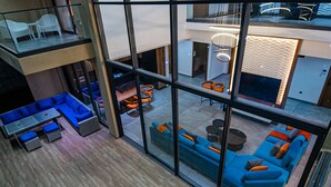 Een modern interieur met een glazen scheidingswand, blauwe banken en oranje kussens.