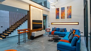 Een moderne woonkamer met een blauwe bank, een televisie en een trap met houten leuningen.