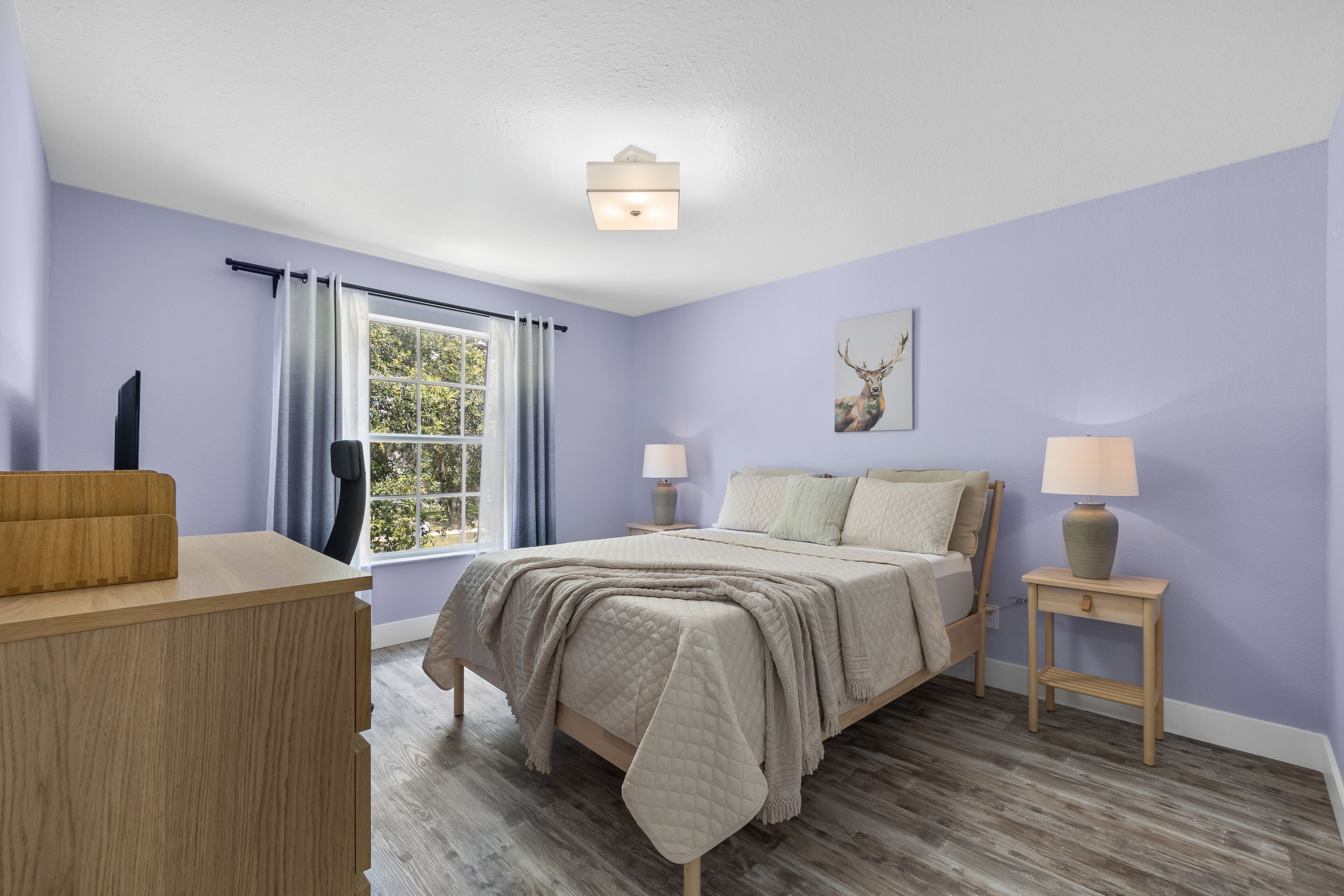 Een slaapkamer met een bed, bedlampen, een raam met gordijnen, een bureau en een wandlamp.