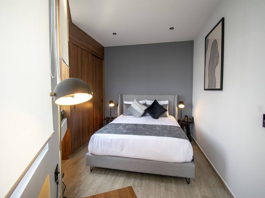 Un dormitorio con cama, lámparas de noche, un armario de madera y un cuadro en la pared.