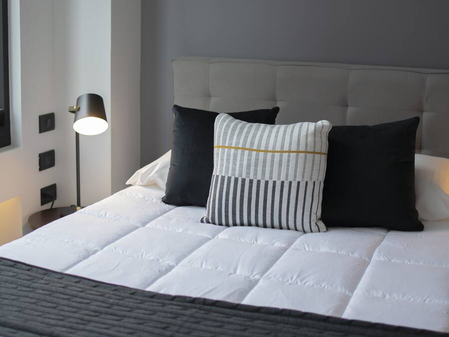 A neatly made bed with a white duvet, black and white striped pillow, and a grey headboard.