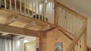 Een houten trap die leidt naar een slaapkamer op een entresol, met een bed en een klein raam.